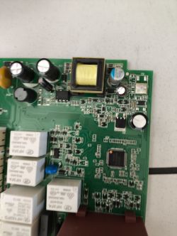 Zbliżenie na zieloną płytkę PCB z komponentami elektronicznymi, w tym cewką i przekaźnikami.