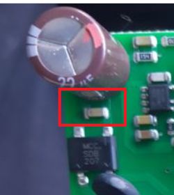 Zbliżenie płytki PCB z dużym kondensatorem i zaznaczonym na czerwono małym elementem SMD