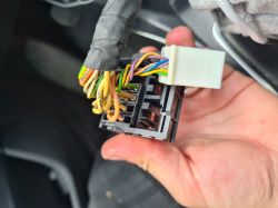 The image shows a close-up of a car wiring harness with a plastic electrical connector held in a hand.