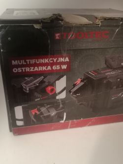 Pudełko ostrzarki wielofunkcyjnej Tooltec 65 W z widocznymi uszkodzeniami opakowania.
