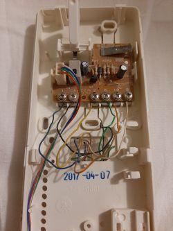 Zdjęcie wnętrza domofonu z widocznymi kolorowymi kablami oraz płytką z elektroniką.