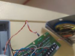 Zbliżenie na oderwany pomarańczowo-biały przewód przy instalacji domofonowej z widoczną płytką drukowaną.