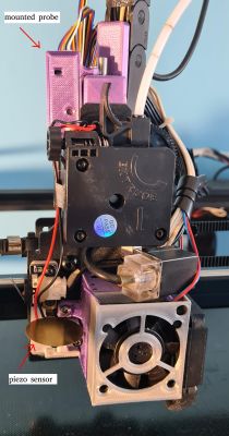Close-up of a 3D printer toolhead with mounted probe and piezo sensor, labeled with arrows