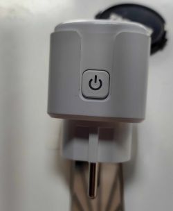 White smart plug with power button on a white wall.