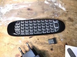 Klawiatura zdalnego sterowania do Smart TV Android Box z odbiornikiem USB i zasilaczem na stole.