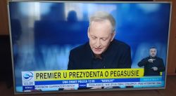 Mężczyzna w studio telewizyjnym z podpisem o tematyce politycznej, przy boku tłumacz języka migowego.