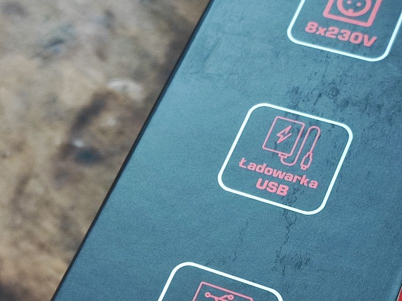Zbliżenie na ikonę z napisem Ładowarka USB na czarnym opakowaniu, obok symbole urządzenia i kabla.
