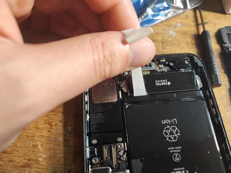 iPhone Battery Replacement - Disassembly Process Hand holding a strip during iPhone battery replacement.