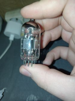 Lampa elektronowa w oprawce metalowo-szklanej trzymana w palcach.