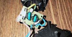 Circuit board inside a disassembled plug; blue, brown, and yellow‑green wires visible.