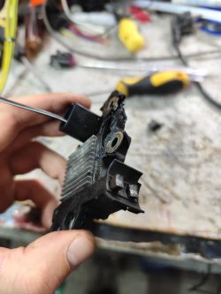 Zużyty regulator napięcia BOSCH z wytartymi szczotkami w ręce technika