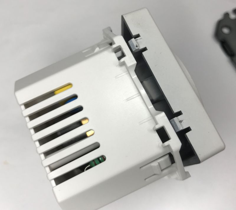 White in-wall outlet with loosened front frame; side ventilation slots visible in close-up