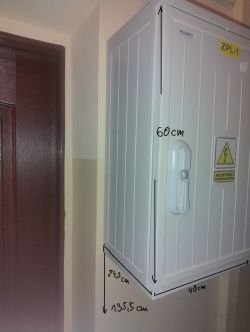 Szafka elektryczna na ścianie obok drzwi z widocznymi wymiarami: 60 cm wysokości, 40 cm szerokości, umieszczona na wysokości 135,5 cm i 24,5 cm od ściany.