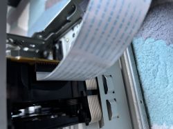 Zbliżenie na taśmę FFC podłączoną do gniazda wewnątrz metalowej obudowy urządzenia elektronicznego.
