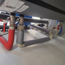 Widok na rurki i zawory instalacji grzewczej podłogowej.