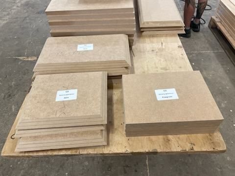 Stosy paneli MDF ułożone na drewnianej platformie w warsztacie.