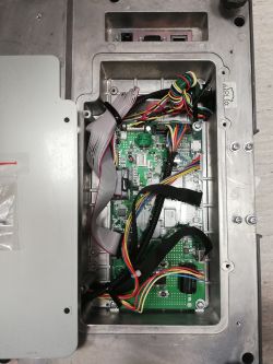 Zbliżenie wnętrza metalowej obudowy z podłączoną płytą PCB i wieloma przewodami.