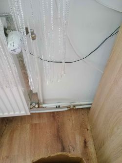 Grzejnik na tle ściany z przewodami i zasłoną z koralików.