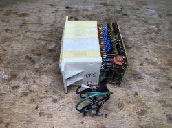 Electronic module with a white housing and PCB with wires, lying on a wooden workbench