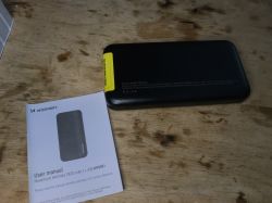 Czarny powerbank Wozinsky WPBBK1 z instrukcją obsługi, leżący na drewnianym stole.