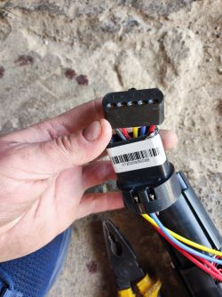 Zbliżenie na wtyczkę z przewodami i oznaczeniami, trzymaną w ręce przy akumulatorze z hulajnogi elektrycznej.