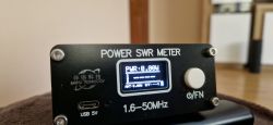 Czarny miernik mocy i SWR 1,6–50 MHz z małym ekranem i pokrętłem, zasilanie USB 5V.