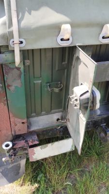 Otwarta klapka w tylnej części zielonego pojazdu, z widocznym gniazdem elektrycznym i zaczepami.