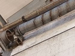 Sprężyna skrętna w mechanizmie bramy garażowej, z widoczną zębatką.