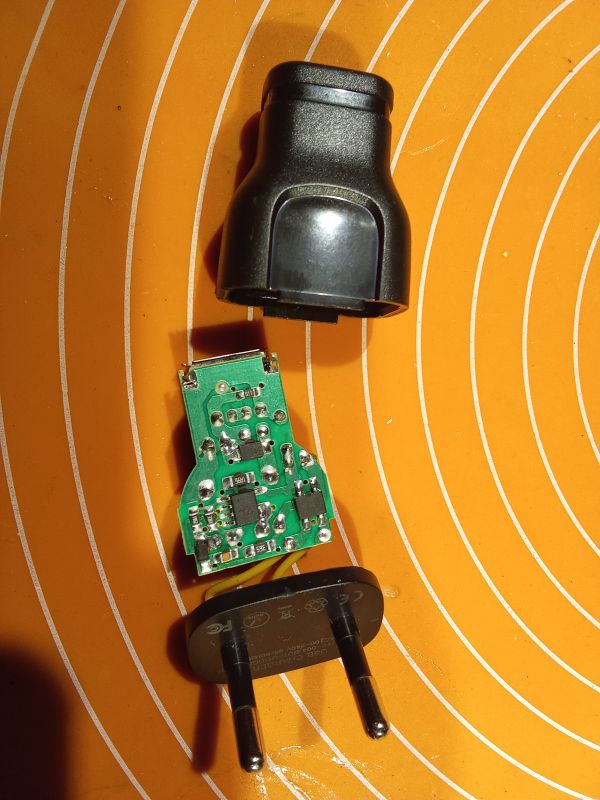 Rozebrana mała ładowarka USB z widoczną płytką PCB i gniazdem elektrycznym