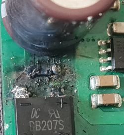 Zbliżenie płytki PCB z nadpalonym obszarem obok kondensatora i mostka prostowniczego DB207S