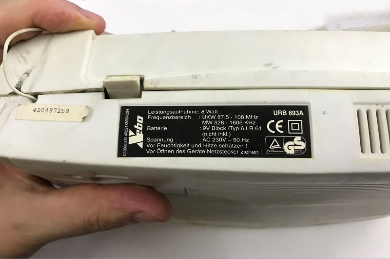 Nameplate label “URB 693A” on the underside of a white device, held in hands