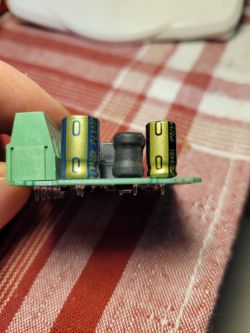 Close-up of a PCB with a green terminal block, two capacitors, and a black inductor on a red checkered cloth.