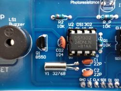 Close-up of a PCB showing DS1302 IC, 32.768 kHz crystal, buzzer, and 10 kΩ resistors