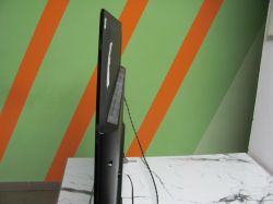 Monitor z widocznymi przewodami na tle zielonej ściany z pomarańczowymi pasami.