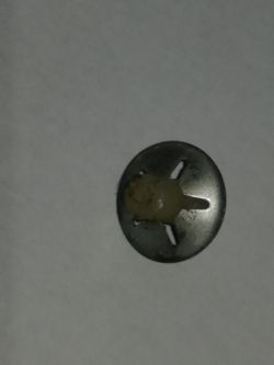 Mały metalowy element z plastikowym środkiem, leżący na jasnym tle.