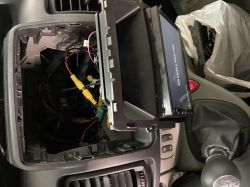 Widok z wnętrza samochodu z wyjętym panelem sterowania i widocznymi przewodami elektrycznymi.