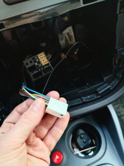 Osoba trzymająca złącze elektryczne z kolorowymi przewodami w samochodzie.