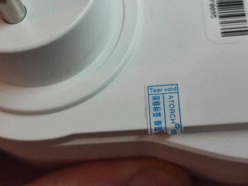 Warranty Seal on Measurement Device Close-up of a warranty seal with the text Tear void on a plug-in energy meter.