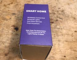 Smart Home Socket Box with Reset Instruction Purple smart home product box with reset instruction on a wooden surface.