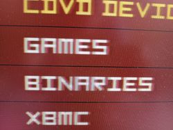 Rozmazany ekran z menu “GAMES”, “BINARIES”, “XBMC” na czerwonym tle.