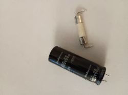 Spalony bezpiecznik i kondensator 400V 68uF leżą na jasnym tle.