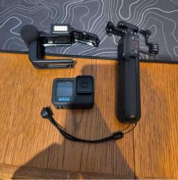 Kamera GoPro z akcesoriami: statyw, obudowa z mikrofonem i lampą LED na drewnianym stole.