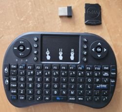 Mała, bezprzewodowa klawiatura z touchpadem, adapterem USB i osłoną Dell na drewnianym stole.
