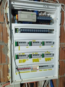 Rozdzielnia elektryczna z programowalnym sterownikiem PLC i przekaźnikami, widoczna w budynku.