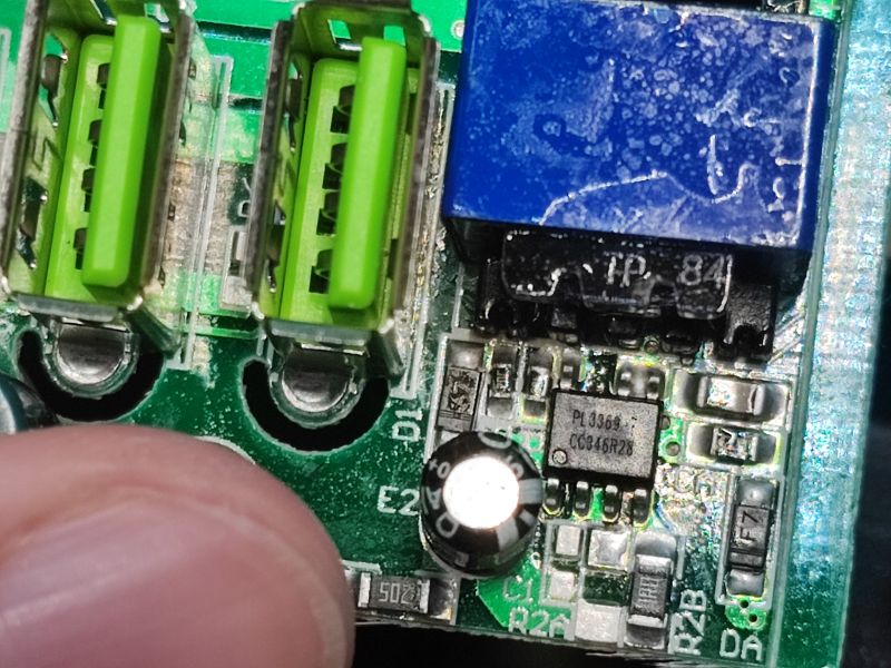 Zbliżenie na płytkę drukowaną z dwoma portami USB, niebieskim transformatorem oraz układem scalonym PL3369.