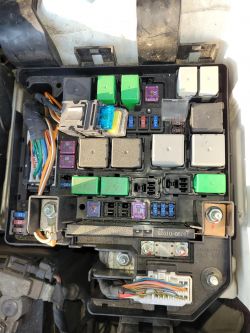 Widok wnętrza skrzynki bezpiecznikowej w samochodzie, z różnymi bezpiecznikami i przekaźnikami.