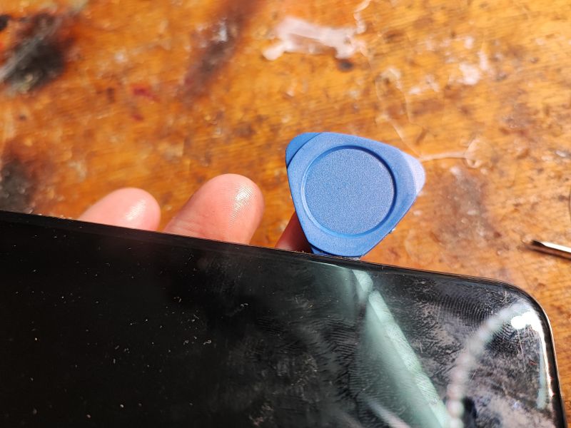 Opening a Smartphone with a Plastic Tool Smartphone being opened with a flat plastic tool on a wooden table.