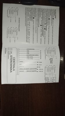 Instrukcja montażu sterownika centralnego zamka z opisem kabli i schematem podłączeń, leżąca na drewnianym stole.