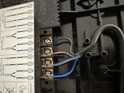 Zbliżenie na złącze elektryczne płyty indukcyjnej IKEA z widocznym schematem podłączenia i przewodami: czarnym, brązowym, niebieskim oraz szarym.
