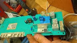 Moduł elektroniczny pralki z wymienionym triakiem, trzymany w dłoni, widoczne przekaźniki i radiator.